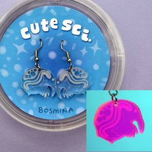 May include: Clear acrylic earrings with a jellyfish design, displayed on a blue card inside a clear plastic container. The card has the text "cute sci." and "BOSMINA". A small, pink and orange charm with a similar design is also shown.