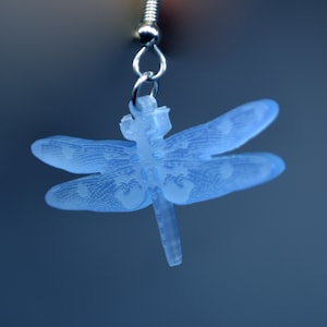 Op de afbeelding: Lichtblauwe libellen oorbellen met gedetailleerde vleugelpatronen. De oorbellen hangen aan een zilverkleurige haak. Een delicaat, door de natuur geïnspireerd accessoire.