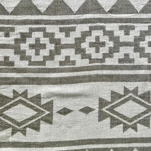 May include: A close-up of a white and gray patterned textile. The design features geometric shapes, including triangles, diamonds, and crosses, arranged in horizontal bands. The fabric has a textured appearance.