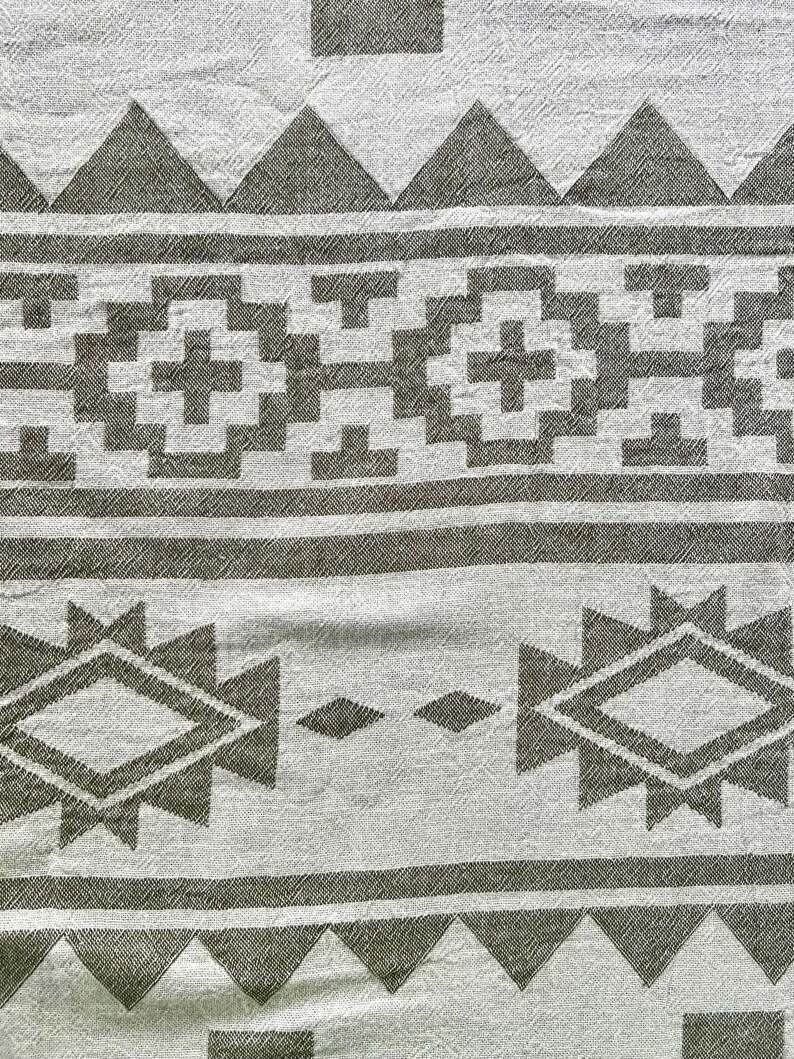 May include: A close-up of a white and gray patterned textile. The design features geometric shapes, including triangles, diamonds, and crosses, arranged in horizontal bands. The fabric has a textured appearance.