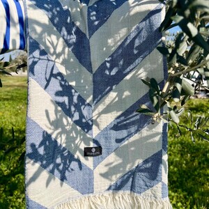 May include: A blue and white chevron patterned blanket with fringe. The blanket is draped over a tree branch. The blanket has a tag that says "masumi".