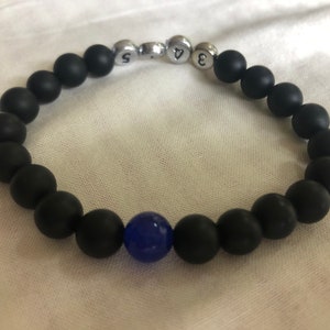 May include: Black beaded bracelet with a single blue bead and silver number beads. The bracelet is made of matte black beads and has a stretchable design. The numbers on the silver beads are 3, 4, and 5.
