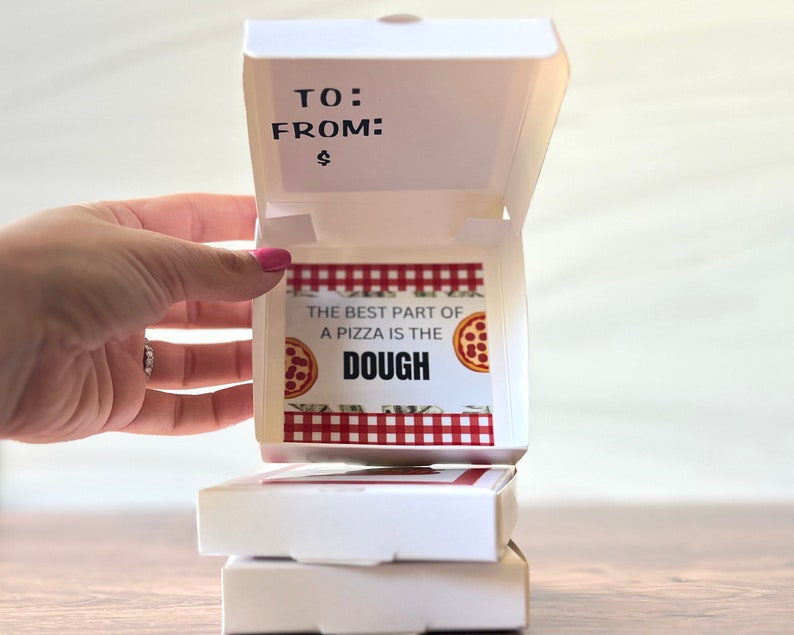 May include: A white pizza box with a red and white checkered pattern and the text "The best part of a pizza is the dough" with a small pizza graphic. The box is open and the top is folded back.