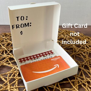 May include: White cardboard box with a red and white checkered pattern inside. The box is open and has a blank space for writing "To:" and "From:". The box also has a space for writing a dollar amount. The box has a label that says "Gift Card not included".