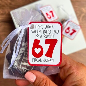 May include: A Valentine's Day gift bag with a tag that reads "Hope your Valentine's Day is a sweet 67" with a heart. The bag contains candy bars. The tag also says "From: Jonah".