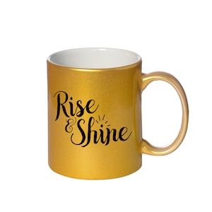 May include: A gold ceramic coffee mug with a black inscription that reads "Rise & Shine".