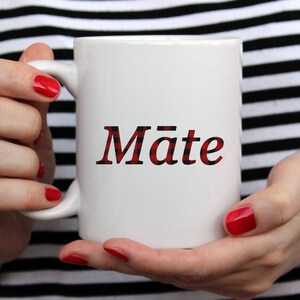 May include: White ceramic mug with a red and black plaid design that says "Mate" in red.