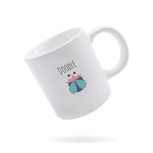 May include: White ceramic mug with a whimsical insect illustration and the word "DOODLE". The insect has pink, blue, and teal accents. The mug has a curved handle and is set against a white background.