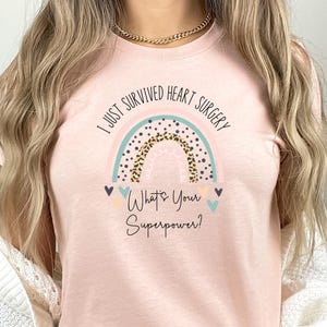 May include: A pink t-shirt with a rainbow graphic and the text "I just survived heart surgery. What's your superpower?"