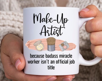 Può includere: Tazza in ceramica bianca con una grafica in bianco e nero che dice "Make-Up Artist because badass miracle worker isn't an official job title". La grafica include anche un pennello per il trucco, un compatto e un blush.