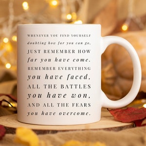Puede incluir: Taza de cerámica blanca con una cita motivacional: "Siempre que te encuentres dudando de lo lejos que puedes llegar, recuerda simplemente lo lejos que has llegado. Recuerda todo lo que has enfrentado, todas las batallas que has ganado y todos los miedos que has superado."