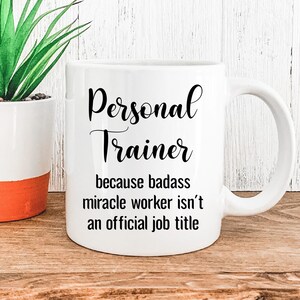 May include: White ceramic coffee mug with black text that reads "Personal Trainer because badass miracle worker isn't an official job title."
