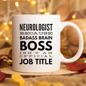 May include: White ceramic coffee mug with black text that reads "Neurologist because badass brain boss isn't an official job title".