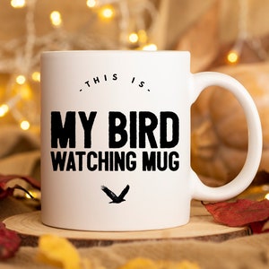 May include: White ceramic mug with black text that reads "This is my bird watching mug" and a black silhouette of a bird flying.