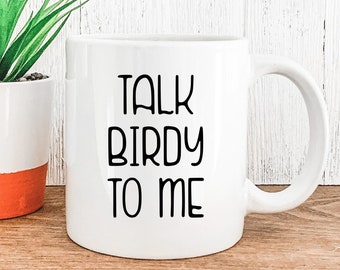 Puede incluir: Taza de café de cerámica blanca con texto negro que dice "Talk Birdy To Me".