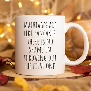 May include: White ceramic coffee mug with black text that reads "Marriages are like pancakes. There is no shame in throwing out the first one."