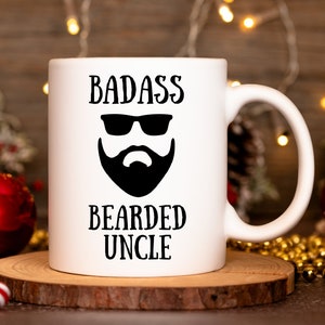 May include: White ceramic mug with the words "BADASS BEARDED UNCLE" in black, along with a graphic of a beard and sunglasses. The mug is on a wooden coaster, with a blurred background of Christmas decorations.