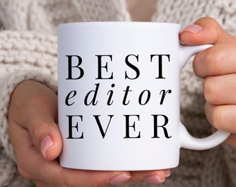 Może przedstawiać: Biały kubek ceramiczny z czarnym napisem "BEST editor EVER".