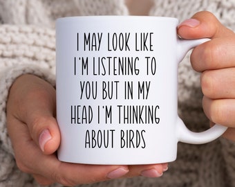May include: White ceramic mug with black text that reads "I may look like I'm listening to you but in my head I'm thinking about birds."