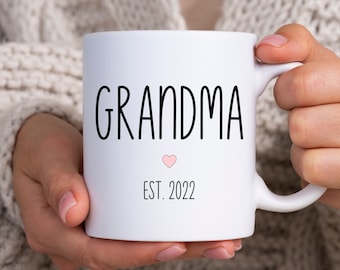 May include: White ceramic mug with black text that reads "Grandma Est. 2022" and a small pink heart.