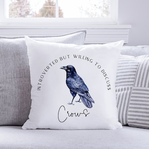Op de afbeelding: Een wit kussen met een zwarte kraai-illustratie en de tekst "Introvert maar bereid om over kraaien te praten".