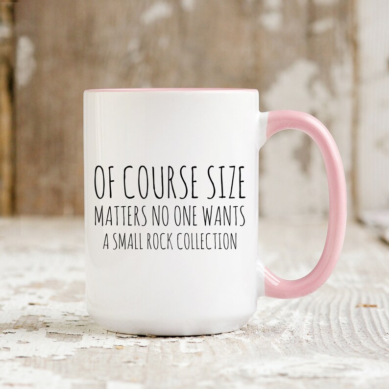 May include: White ceramic coffee mug with a pink rim and handle. The mug has black text that reads "Of course size matters no one wants a small rock collection."