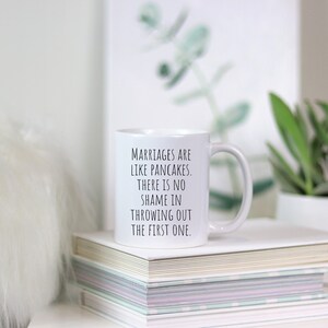 May include: White ceramic coffee mug with black text that reads "Marriages are like pancakes. There is no shame in throwing out the first one."