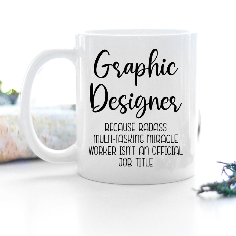 May include: White ceramic coffee mug with a black graphic that reads "Graphic Designer because badass multi-tasking miracle worker isn't an official job title."