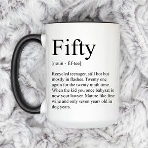 May include: White ceramic mug with a black handle and black rim. The mug has black text that reads "Fifty [noun - fif-tee] Recycled teenager, still hot but mostly in flashes. Twenty one again for the twenty ninth time. When the kid you once babysat is now your lawyer. Mature like fine wine and only seven years old in dog years."