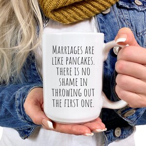 May include: White ceramic mug with a black text saying "Marriages are like pancakes. There is no shame in throwing out the first one."