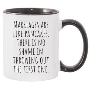 May include: White ceramic coffee mug with a black rim and handle. The mug has a funny saying printed on it: "Marriages are like pancakes. There is no shame in throwing out the first one."