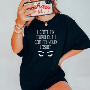 May include: Black t-shirt with the text "I can't fix stupid but I can fix your lashes" and a stylized illustration of eyelashes.