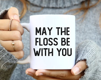 May include: White ceramic mug with black text that reads "May the floss be with you".