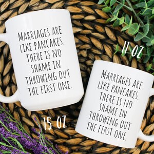 May include: Two white ceramic mugs with black text that reads "Marriages are like pancakes. There is no shame in throwing out the first one." The mug on the left is 15 oz and the mug on the right is 11 oz.