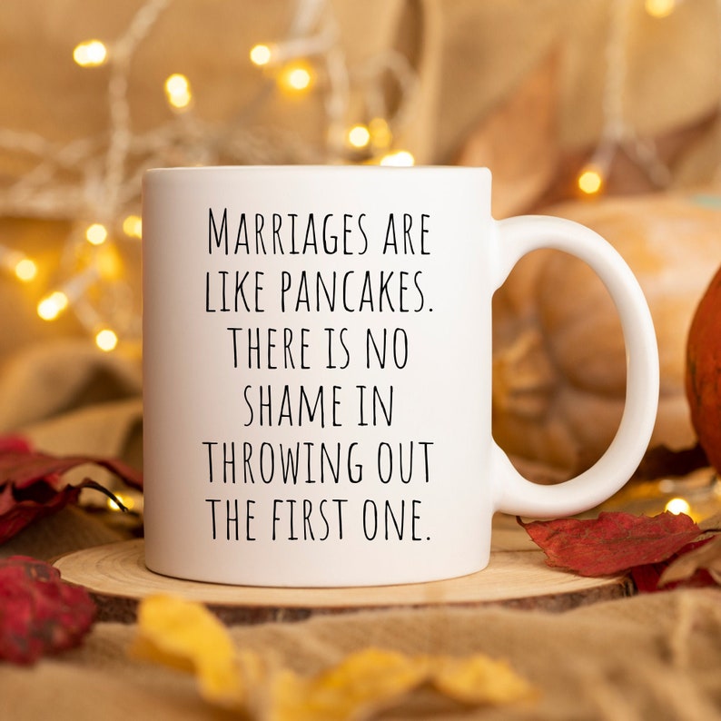 May include: White ceramic coffee mug with black text that reads "Marriages are like pancakes. There is no shame in throwing out the first one."