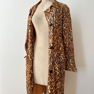 Puede incluir: Un abrigo largo con estampado de leopardo, botones negros y cuello. El abrigo se exhibe en un maniqu&iacute; sobre un fondo blanco. El patr&oacute;n del abrigo presenta manchas marrones y beige.
