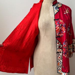May include: A red silk jacket with floral embroidery and a mandarin collar. The jacket is open to reveal a red silk lining.
