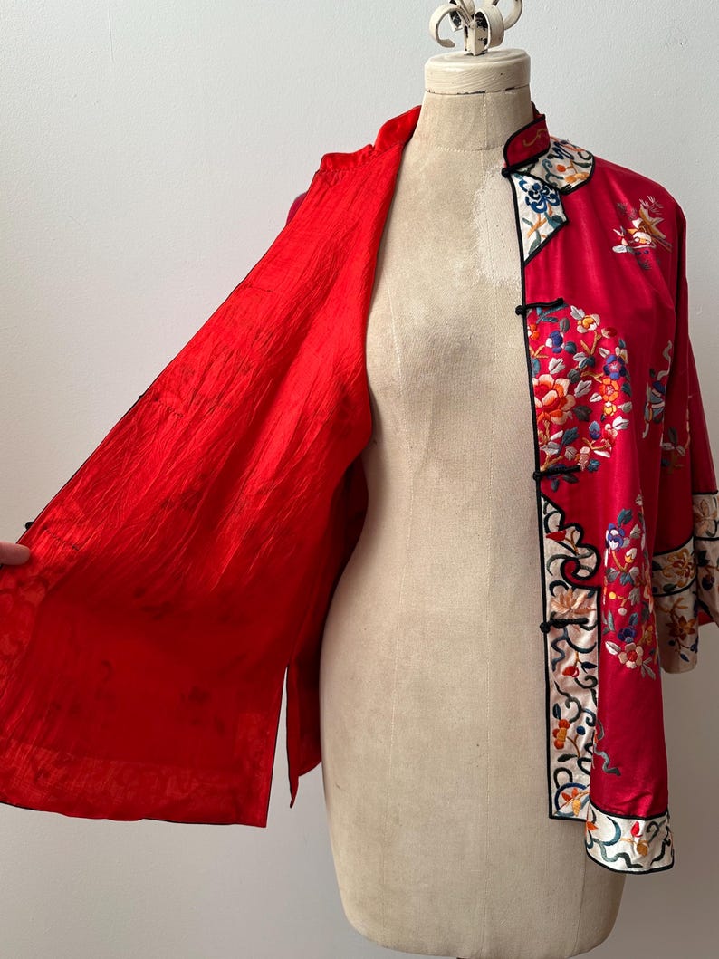 May include: A red silk jacket with floral embroidery and a mandarin collar. The jacket is open to reveal a red silk lining.