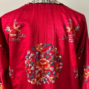 May include: A red silk robe with intricate floral embroidery in shades of blue, green, orange, and yellow. The robe has a mandarin collar and is adorned with birds and flowers.