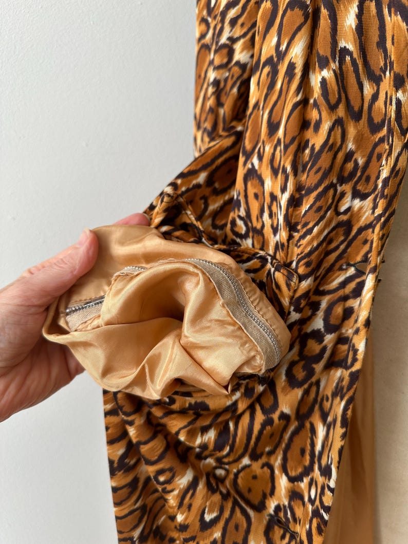 Puede incluir: Primer plano de una prenda con estampado de leopardo en tonos marrones y negros. El forro interior es de color beige liso. El pu&ntilde;o de la manga es visible, con un detalle de cremallera.