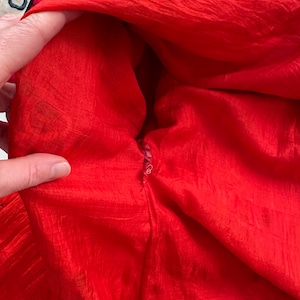 May include: Close-up of the inside of a red garment with a zipper. The fabric is a silky, crinkled material.