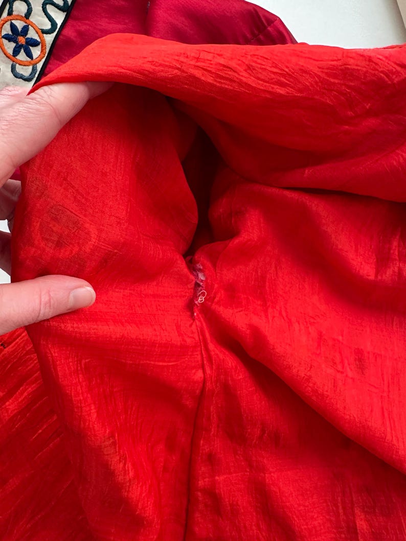 May include: Close-up of the inside of a red garment with a zipper. The fabric is a silky, crinkled material.