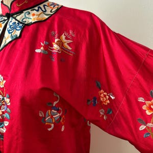 May include: A red silk robe with intricate floral embroidery in shades of blue, green, yellow, and pink. The robe has a mandarin collar with a black trim and a white and blue embroidered design.