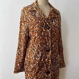 Puede incluir: Un abrigo de manga larga con estampado de leopardo en tonos marr&oacute;n y beige. El abrigo tiene cuello y botones negros. La prenda se exhibe en un maniqu&iacute;. Se aprecia la longitud del abrigo.