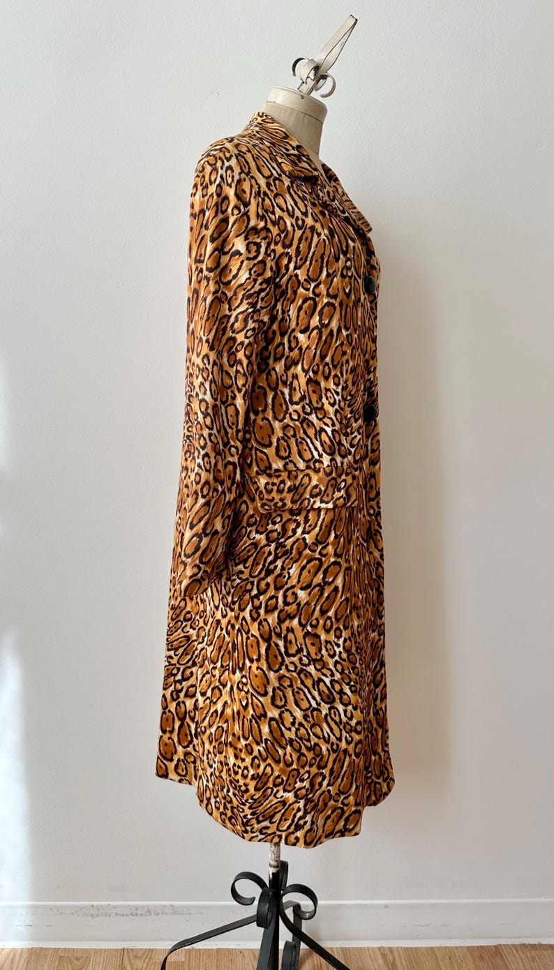 Puede incluir: Un abrigo largo con estampado de leopardo con cuello cl&aacute;sico y mangas largas. El abrigo presenta un estampado de manchas marrones y beige y se exhibe en un maniqu&iacute;. El abrigo tiene cierre de botones y bolsillos.