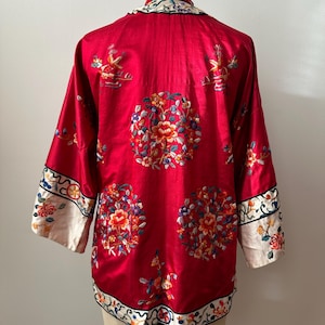 May include: A red silk Chinese robe with white trim and intricate floral embroidery. The robe has a mandarin collar and long sleeves.