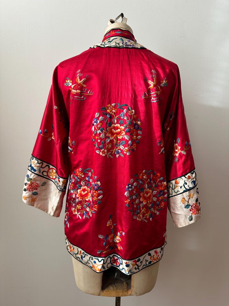 May include: A red silk Chinese robe with white trim and intricate floral embroidery. The robe has a mandarin collar and long sleeves.