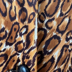 Puede incluir: Primer plano de una prenda con un estampado animal audaz en tonos marrones, beige y negro. La tela tiene una apariencia texturizada. Se ve un bot&oacute;n negro ovalado grande en la parte inferior, sujeto con hilo negro.