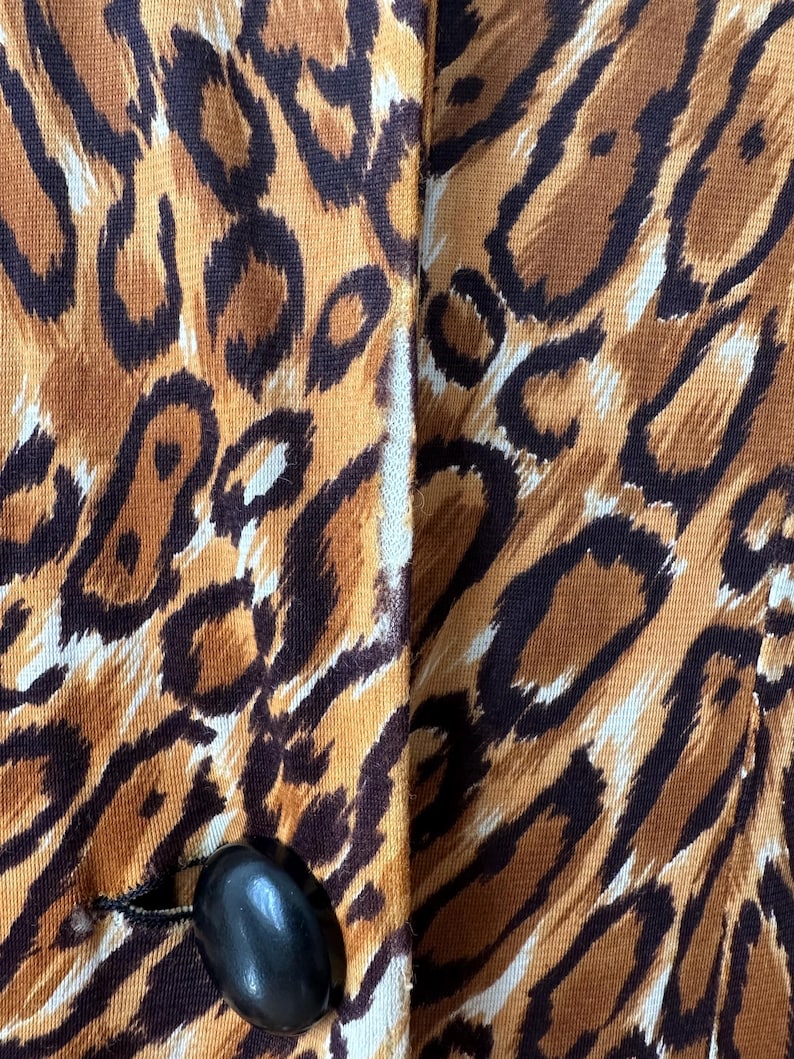 Puede incluir: Primer plano de una prenda con un estampado animal audaz en tonos marrones, beige y negro. La tela tiene una apariencia texturizada. Se ve un bot&oacute;n negro ovalado grande en la parte inferior, sujeto con hilo negro.