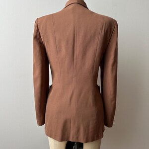 May include: A brown blazer displayed on a mannequin. The tailored jacket features a notched lapel, two front pockets, and a fitted silhouette. The back view highlights the structured design and the warm, earthy tone of the fabric.